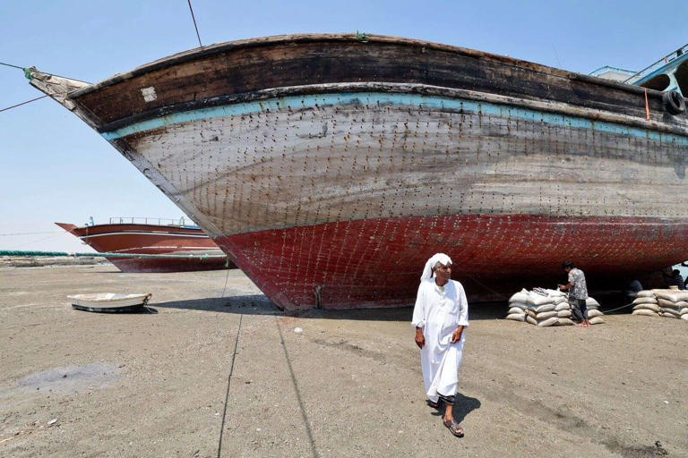مردی در 29 آوریل 2023 در جزیره توریستی قشم در خلیج فارس در مقابل یک کشتی سنتی چوبی (لنج) که برای بازسازی در ساحل گذاشته شده است، قدم می زند. — خبرگزاری فرانسه